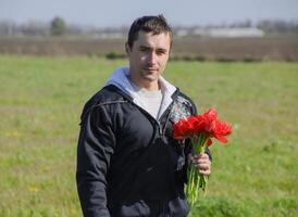 un' uomo nel un' giacca su un' campo di tulipani. radura con tulipani. un' uomo è strappo tulipani nel un' mazzo foto