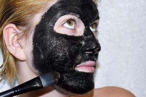 ragazza nel un' cosmetico nero maschera. detergente maschera di aspirina e attivato carbonio. nero cosmetico viso maschera. foto