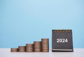 2024 scrivania calendario e pila di monete. il concetto di Salvataggio i soldi, finanziario, investimento e attività commerciale in crescita nel nuovo anno 2024. foto