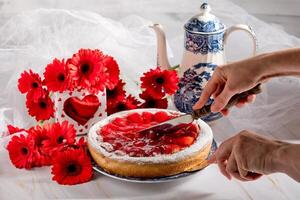 ancora vita, mano tagliare fragola torta su un' tavolo decorato con rosso gerbere per La madre di giorno foto