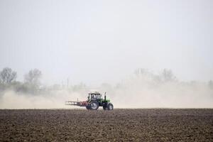 il trattore erpici il suolo su il campo e crea un' nube di polvere dietro a esso foto