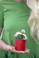 un' bionda ragazza con lungo capelli nel un' luminosa verde vestito Tenere un' rosso boccale foto