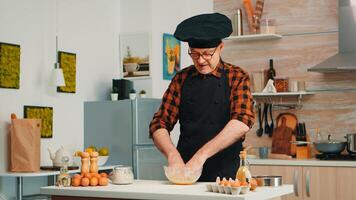 panettiere kending Impasto nel cucina tavolo indossare grembiule e bonete. pensionato anziano capocuoco con uniforme aspersione, setacciare vagliatura crudo ingredienti di mano cottura al forno fatti in casa Pizza, pane. foto