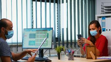 donna con protettivo maschera digitando su Telefono mentre collega Lavorando utilizzando appunti rispetto sociale distanziamento. libero professionista nel nuovo normale ufficio chat scrittura su mobile con Internet tecnologia foto