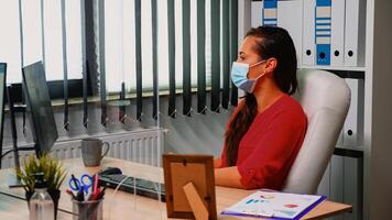 attività commerciale donna con maschera protezione analizzando annuale grafici seduta nel ufficio rispetto sociale distanziamento. libero professionista Lavorando nel nuovo normale ufficio discutere chat avendo virtuale in linea conferenza foto