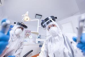 pov di paziente nel dentale ufficio ottenere trattamento a partire dal dentista squadra condurre al di sopra di per opera su denti cavità. stomatologia squadra indossare sicurezza attrezzatura contro coronavirus trattamento paziente. foto