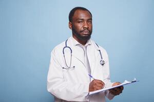 africano americano medico professionista afferrare un' appunti mentre guardando a il telecamera. nero maschio medico residente Tenere pazienti grafici e documenti mentre in piedi contro isolato sfondo. foto