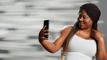 africano americano donna in posa su smartphone telecamera, recitazione sciocco e mostrando corpo fiducia. contento bellissimo ragazza essere sensuale e naturale, esprimendo se stesso corpo accettazione. foto