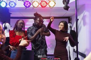 gruppo musicale frontman cantando e diverso donne danza su palcoscenico a discoteca nel discoteca. spensierato musicisti utilizzando dj stazione e microfono mentre l'esecuzione a club discoteca festa foto