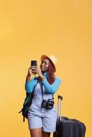 viaggiatore assunzione fotografie su mobile Telefono con carrello borse e bagaglio, scappa viaggio. femmina turista utilizzando smartphone per prendere immagini su internazionale vacanza viaggio, divertente ragazza.