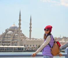 un' giovane viaggiatore con un' zaino su sua indietro sembra a il telecamera nel davanti di un' moschea nel Istanbul. foto