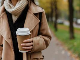 ai generato ritagliata Immagine di giovane donna potabile porta via caffè mentre a piedi nel autunno parco. selettivo messa a fuoco su tazza foto