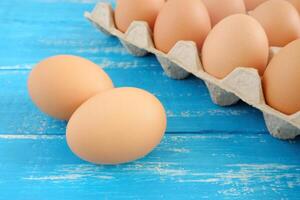 fresco pollo uova e uovo scatola di cartone su blu afflitto di legno tavolo foto