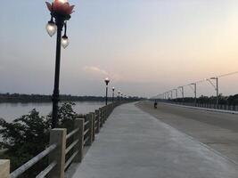 ponte e tramonto Là è un' lungo fiume sera cielo, un' leggero polo su il lato di il strada. foto