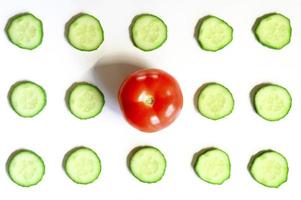 schema ripetuto di semicerchi affettati di cetrioli di verdure crude fresche per insalata e un pomodoro intero foto