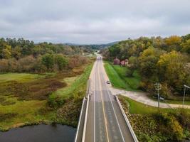 ponte sul fiume con strada rurale in autunno con erba verde e ombre di alberi dalle montagne servono la strada che entra in autostrada foto