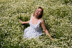 un' donna nel un' bianca vestito con polka puntini è su un' radura con margherite. fioritura margherite foto