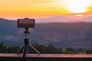 un' smartphone è registrazione il sole ambientazione al di sopra di un' montagna gamma. foto