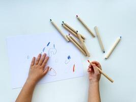 piccolo bambino disegna con colorato matite su carta su bianca tavolo. foto