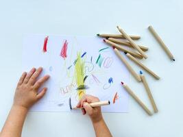 piccolo bambino disegna con colorato matite su carta su bianca tavolo. foto