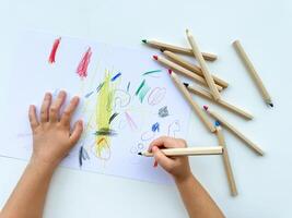 piccolo bambino disegna con colorato matite su carta su bianca tavolo. foto