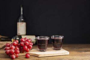 un' mazzo di rosso uva con rosso uva succo nel un' bicchiere posto su un' di legno tavolo o rosso vino, delizioso naturale salutare succo bere. foto