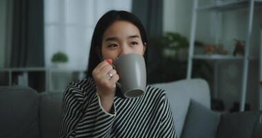 ritratto di rilassante giovane donna Tenere tazza godere odore caffè o tè e potabile con felicità nel mattina mentre sedersi su divano nel vivente stanza, libera tempo, prendi rompere nel a casa, sorridente foto