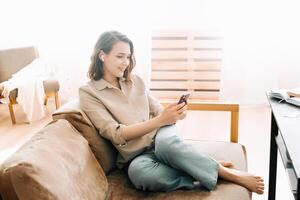 lieto del Millennio donna nel senza fili cuffie sembra a Telefono, legge messaggi, gode chattare. comunicazione, digitale stile di vita, e tecnologia felicità concetto. senza fili connessione beatitudine. foto