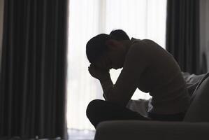 silhouette di un' persona sofferenza a partire dal depressione nel il Casa, depresso donna seduta solo su il divano sentire fatica, triste e preoccupato nel il buio camera. persona siamo stressato. foto