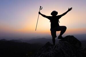 silhouette di un' scalatore a il superiore di il roccioso montagna a tramonto, uomo su superiore di montagna. concettuale design. solo a il vertice scalatore riuscito scalatori. sport e attivo vita. foto