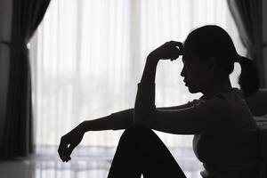 silhouette di un' persona sofferenza a partire dal depressione nel il Casa, depresso donna seduta solo su il divano sentire fatica, triste e preoccupato nel il buio camera. persona siamo stressato. foto