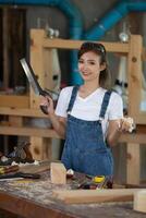 giovane donna è formazione per essere un' falegname nel officina. falegname Lavorando con attrezzatura su di legno tavolo. donna lavori nel un' carpenteria negozio. foto