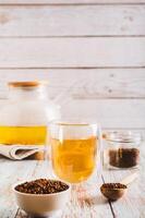 fresco grano saraceno tè nel un' bicchiere e teiera e granuli nel un' ciotola su il tavolo verticale Visualizza foto