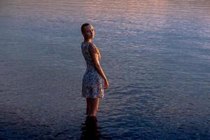 adolescente ragazza nel un' vestito di il mare entra il acqua foto