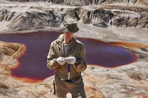 geologo esamina un' campione di minerale nel il deserto contro il sfondo di un' sale lago foto