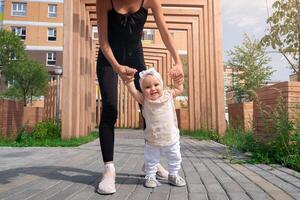 bambino piccolo bambino ragazza con mamma camminare nel il città cortile, bambino impara per camminare foto