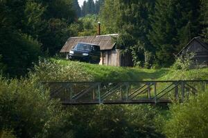 rurale paesaggio, un' solitario fattoria nel il foresta - un' log cabina, un' stabilimento balneare e un suv su il bordo di un' burrone con un' ponte foto