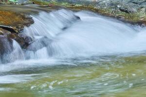 chiaro ruscello flussi al di sopra di il pietre formatura un' piccolo cascata foto