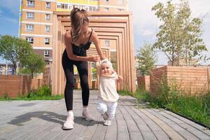 mamma e bambino piccolo figlia camminare nel il città cortile, bambino impara per camminare foto