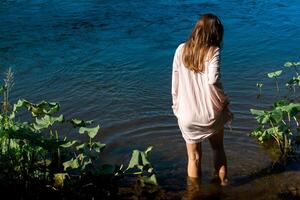 giovane donna passeggiate in il fiume per bagnarsi nel un' camicia foto