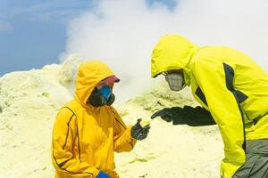 vulcanologi su il pendenza di il vulcano studia campioni di minerali contro il fondale di fumo zolfo fumarole foto