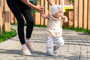 mamma e bambino piccolo figlia camminare nel il città cortile, bambino impara per camminare foto