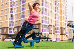 giovane donna scuote sua indietro muscoli nel il città cortile utilizzando strada esercizio macchina iper estensione panchina foto