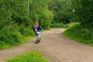 giovane donna cavalcate un elettrico scooter lungo il sentiero nel il parco foto