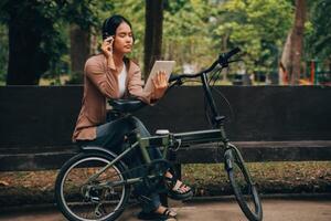 contento giovane asiatico donna mentre equitazione un' bicicletta nel un' città parco. lei sorrise utilizzando il bicicletta di trasporto. l'ambiente amichevole concetto. foto