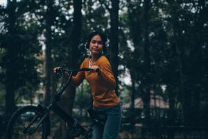 contento giovane asiatico donna mentre equitazione un' bicicletta nel un' città parco. lei sorrise utilizzando il bicicletta di trasporto. l'ambiente amichevole concetto. foto