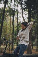 contento asiatico giovane donna camminare e cavalcata bicicletta nel parco, strada città sua sorridente utilizzando bicicletta di trasporto, eco amichevole, persone stile di vita concetto. foto