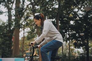 contento asiatico giovane donna camminare e cavalcata bicicletta nel parco, strada città sua sorridente utilizzando bicicletta di trasporto, eco amichevole, persone stile di vita concetto. foto