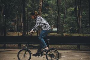 contento asiatico giovane donna camminare e cavalcata bicicletta nel parco, strada città sua sorridente utilizzando bicicletta di trasporto, eco amichevole, persone stile di vita concetto. foto