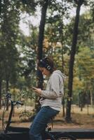 contento asiatico giovane donna camminare e cavalcata bicicletta nel parco, strada città sua sorridente utilizzando bicicletta di trasporto, eco amichevole, persone stile di vita concetto. foto